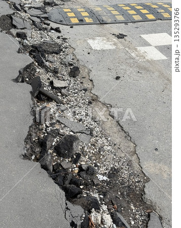 Damaged asphalt road with cracked surface showing exposed gravel and debris 135293766