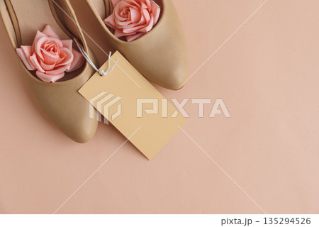 Beige High Heels with Roses and Gift Tag on Peach Background Beige High Heels with Roses and Gift Tag on Peach Background 135294526