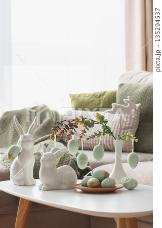 Cozy Easter Living Room Decor with Bunny Figurines and Hanging Eggs on White Table 135294537