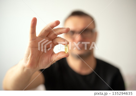 Man holding omega 3 soft gel capsule in his hand Man holding omega 3 soft gel capsule in his hand 135294635