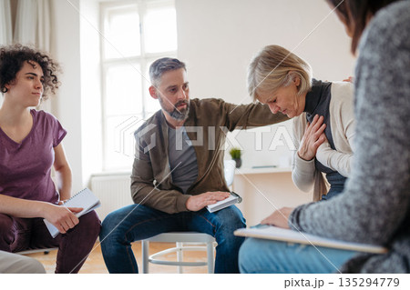 Group of people sitting in a circle and sharing experiences during guided therapeutic session. 135294779