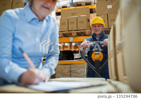 Senior woman manager and man worker working in a warehouse. Senior woman manager and man worker working in a warehouse. 135294786