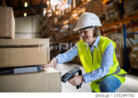 Senior warehouse woman worker working with barcode scanner. 135294792