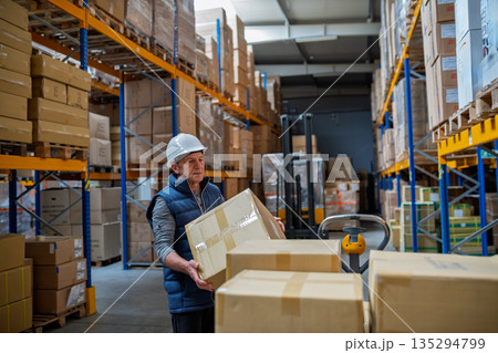 Older male warehouse worker pulling a pallet truck. 135294799