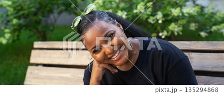 Woman smiling while sitting on bench in park, banner. Natural beauty, confidence, and relaxed mood through outdoor lifestyle portrait 135294868