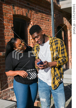 Couple checking smartphone together near brick building. Digital sharing, relationship interaction, and modern communication through mobile technology 135294891