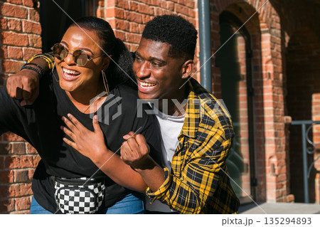 Happy couple laughing together near brick building. Friendship, relationship bonding, and emotional connection through shared moments in urban lifestyle 135294893