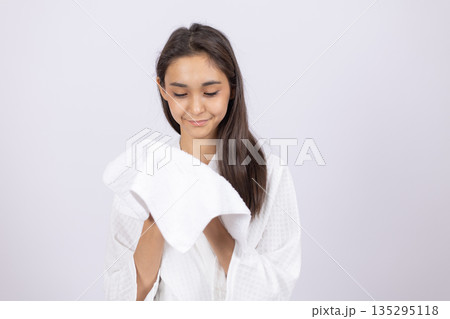Woman in white bathrobe looking at a towel Woman in white bathrobe looking at a towel 135295118