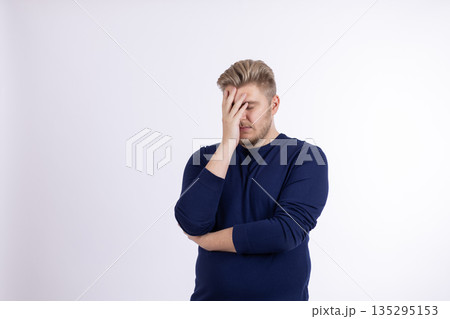 Man in dark blue sweater with hand on forehead 135295153