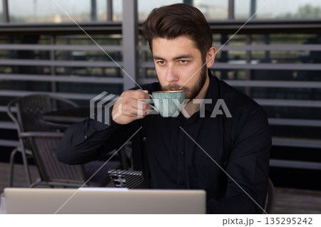 Man in black shirt drinking coffee at outdoor table Man in black shirt drinking coffee at outdoor table 135295242