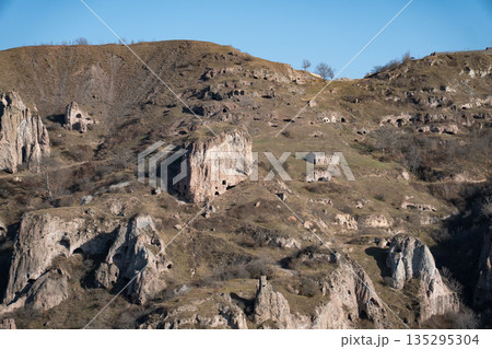 Rocky hills with caves and rugged cliffs in Khndzoresk, Armenia, under a clear blue sky, earthy tones and quiet natural atmosphere 135295304