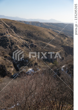 Wide canyon landscape with layered hills and rocky cliffs near Khndzoresk, Armenia, dry grass, stone textures, muted earthy colors under clear light 135295305