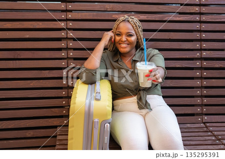 African american woman sipping a drink through a straw while sitting on a bench in the city. Refreshment, relaxation, and simple everyday moments. Banner with copy space African american woman sipping a drink through a straw while sitting on a bench in the city. Refreshment, relaxation, and simple everyday moments. Banner with copy space 135295391
