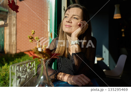 Woman sitting by window in cafe looking into sunlight Woman sitting by window in cafe looking into sunlight 135295469