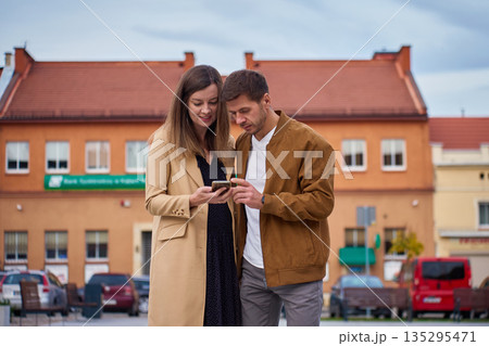 Man and woman checking smartphone while standing in city center Man and woman checking smartphone while standing in city center 135295471