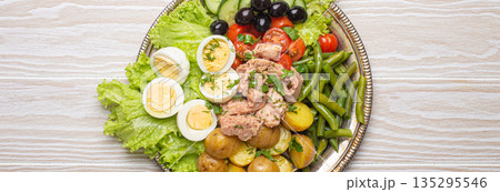 Nicoise salad with tuna, eggs, potatoes, green beans, and olives on a white table Nicoise salad with tuna, eggs, potatoes, green beans, and olives on a white table 135295546