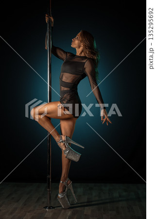 Graceful performer frozen in motion. Choreographed pole dance pose captured in sophisticated studio setting turned striking portrait 135295692