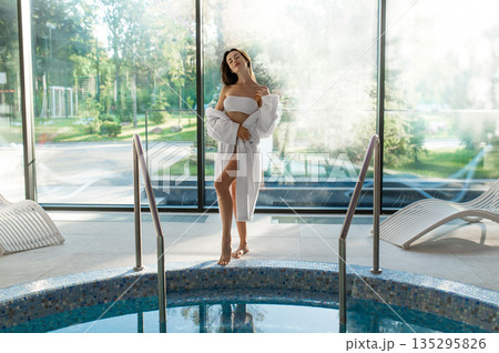 Cute young woman in white bathrobe spending her time at spa center 135295826