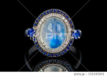 beautiful gold ring with precious stones moonstone, sapphire, diamonds on a black background beautiful gold ring with precious stones moonstone, sapphire, diamonds on a black background 135295941