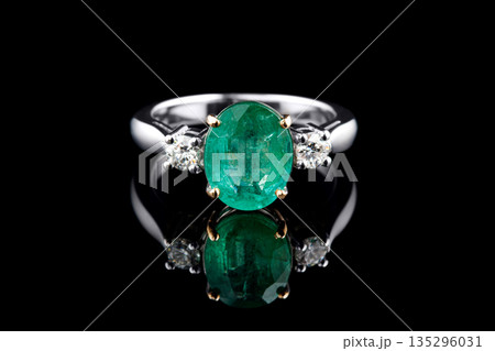 beautiful ring made of gold with precious stones emerald and diamonds on a black background beautiful ring made of gold with precious stones emerald and diamonds on a black background 135296031
