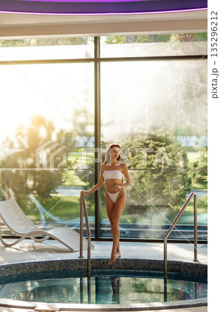 Slim beautiful young woman in white bikini at the swimming pool in spa center Slim beautiful young woman in white bikini at the swimming pool in spa center 135296212