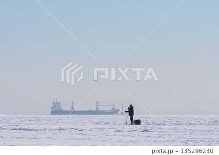 Fisherman on frozen lake preparing place for traditional ice fishing on cold winter snowy day. 135296230