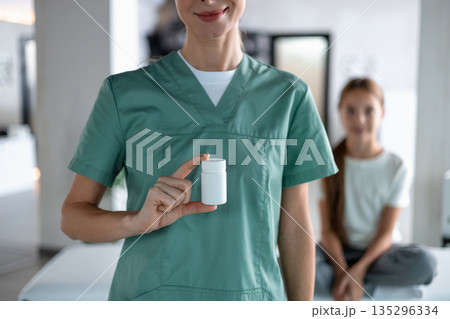 Nurse holding pill bottle in clinic with child patient 135296334
