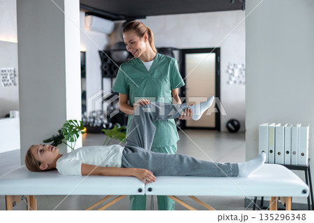 Woman therapist examining little girl leg lying on couch 135296348
