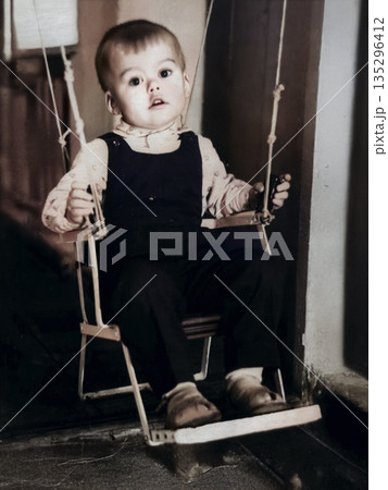 A vintage portrait of a young boy riding on a swing built into a doorway. Photo from 1969. A vintage portrait of a young boy riding on a swing built into a doorway. Photo from 1969. 135296412
