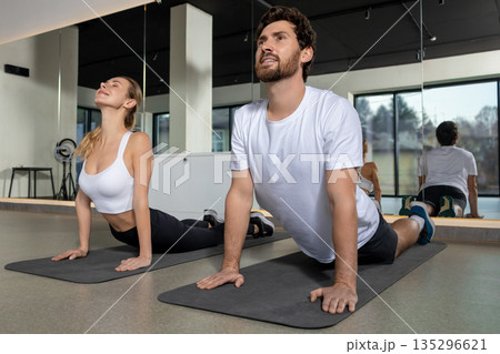 Two friends having a stretching workout in the gym and looking contented Two friends having a stretching workout in the gym and looking contented 135296621