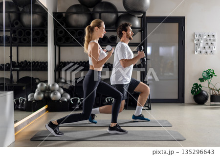 Young man and woman exercising with dumbbells and doing forward lunge 135296643