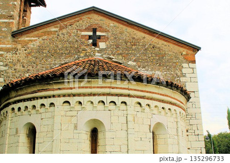 Close-up of the ancient stone apse and decorative arches of the Badia di San Tommaso church. Medieval Romanesque architecture in Brescia, Lombardy, under a clear blue sky. Close-up of the ancient stone apse and decorative arches of the Badia di San Tommaso church. Medieval Romanesque architecture in Brescia, Lombardy, under a clear blue sky. 135296733