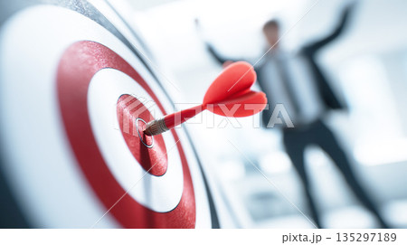 ダーツの的の真ん中に命中した矢と背後でガッツポーズをするビジネスマン 135297189
