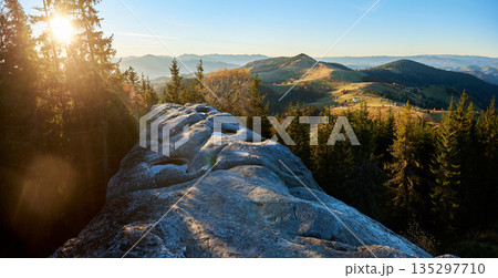 Panoramic image of sunrise over Pysanyi Kamin in Carpathians, Ukraine. Sun's rays illuminating rocky foreground with water-filled depressions. Rolling hills and distant mountain ranges. Panoramic image of sunrise over Pysanyi Kamin in Carpathians, Ukraine. Sun's rays illuminating rocky foreground with water-filled depressions. Rolling hills and distant mountain ranges. 135297710