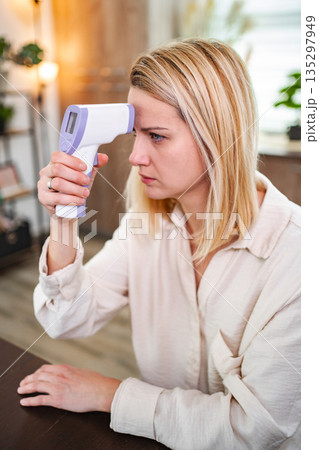 Woman checks her temperature with a digital thermometer at home Woman checks her temperature with a digital thermometer at home 135297949
