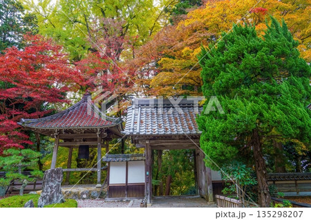 日本の秋の風景：鮮やかな紅葉に包まれた伝統的な寺院の山門と鐘楼 135298207