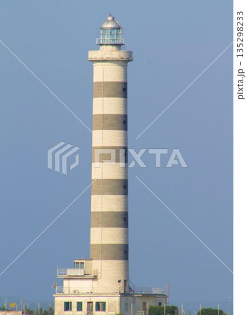 The iconic lighthouse of Lido di Jesolo situated at the mouth of the Sile river. Coastal landscape with the lighthouse tower against a clear sky, a famous landmark of the Venetian Riviera, Italy. The iconic lighthouse of Lido di Jesolo situated at the mouth of the Sile river. Coastal landscape with the lighthouse tower against a clear sky, a famous landmark of the Venetian Riviera, Italy. 135298233