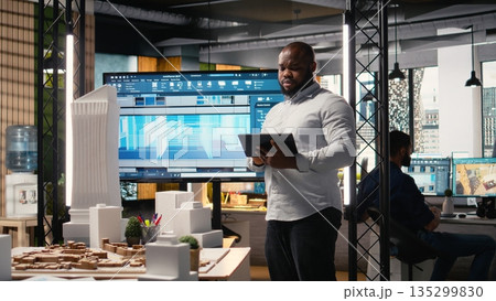 African american real estate developer reviews city planning layout on laptop, setting infrastructure goals while preparing a presentation on sustainable housing urban development. African american real estate developer reviews city planning layout on laptop, setting infrastructure goals while preparing a presentation on sustainable housing urban development. 135299830