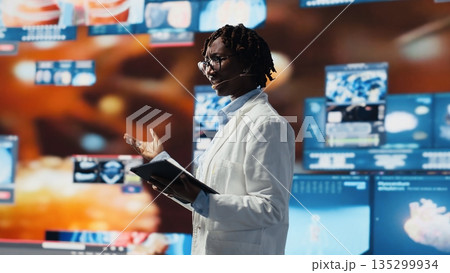 Cheerful woman showing futuristic medical visuals on digital videowall during conference. Jolly African american doctor presenting medical research data and 3D anatomy models dashboards, camera B Cheerful woman showing futuristic medical visuals on digital videowall during conference. Jolly African american doctor presenting medical research data and 3D anatomy models dashboards, camera B 135299934