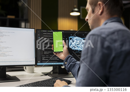 Green screen smartphone used by technician in startup office, optimizing code for performance and scalability. Mockup chroma key phone used by IT worker looking at programming language on PC Green screen smartphone used by technician in startup office, optimizing code for performance and scalability. Mockup chroma key phone used by IT worker looking at programming language on PC 135300116