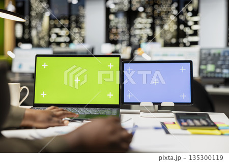 African american CEO at desk uses green screen on laptop and blue screen on tablet, scheduling new meetings and planning the weekly agenda. Business management tasks for a project. 135300119