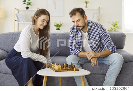 Couple sharing chess moves at home on sofa, playful gestures and smiles together 135302964