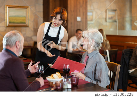 At cafe, Filipino girl waitress communicates with mature couple of customer, accepts order At cafe, Filipino girl waitress communicates with mature couple of customer, accepts order 135303229
