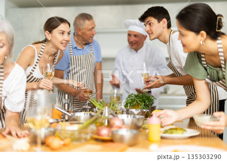 Positive attendees of cooking course talking cheerfully to each other in the kitchen Positive attendees of cooking course talking cheerfully to each other in the kitchen 135303290