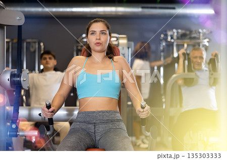 Portrait of young woman during workout with power exercise machine in gym Portrait of young woman during workout with power exercise machine in gym 135303333