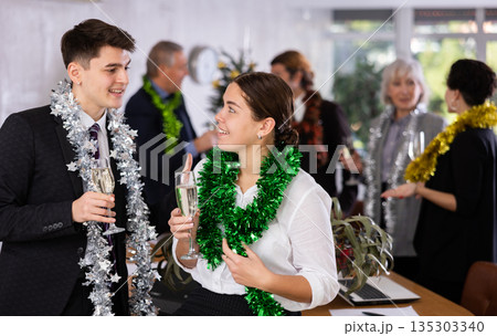 Cheerful young man and woman standing with glasses of champagne during corporate party with colleagues in meeting room 135303340