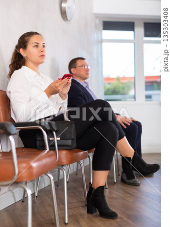 Young woman sitting in line at reception with phone Young woman sitting in line at reception with phone 135303408