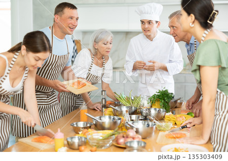 Smiling middle-aged man attendee of cooking course demonstrating piece of salmon on cutting board 135303409