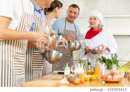 Elderly woman teaching cooking to group of people Elderly woman teaching cooking to group of people 135303413