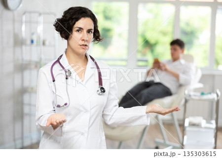 Portrait of female doctor cosmetologist wearing white overall showing equipment of clinic before procedure 135303615